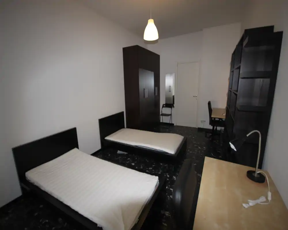 Espaciosa habitación con dos camas individuales, gran armario, escritorio y estanterías — luminosa, amueblada de forma sencilla, ideal para estudiantes o compañeros.