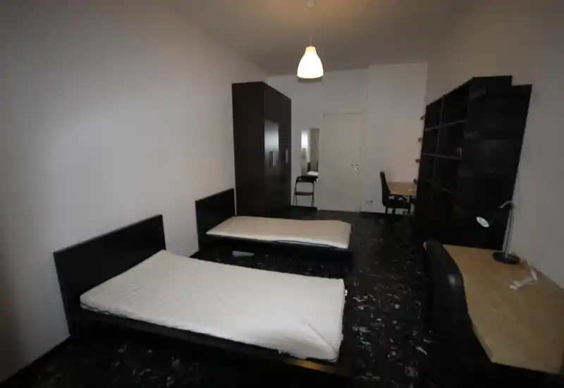 Amplia habitación doble con dos camas individuales, armario y escritorios; estilo minimalista y buena iluminación, apta para anuncios de alquiler.