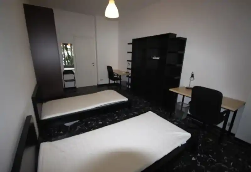 Dormitorio funcional y luminoso con dos camas individuales, dos escritorios y una gran estantería — distribución práctica para compañeros o estudiantes.