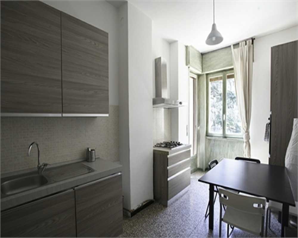 Cocina funcional con armarios efecto madera, fregadero de acero y una pequeña mesa junto a la ventana luminosa: un espacio práctico y bien iluminado para comer.