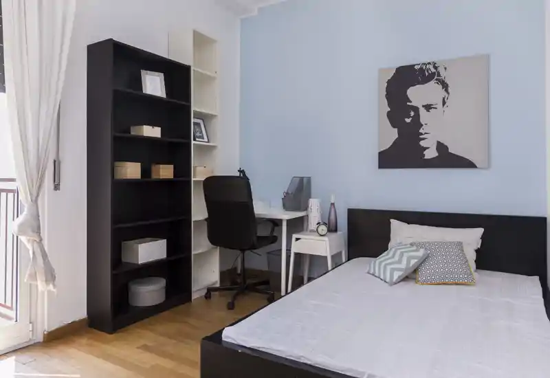 Dormitorio individual moderno y luminoso con cama visible, mesita, escritorio y estantería; buena luz natural y decoración cuidada para mayor confort.