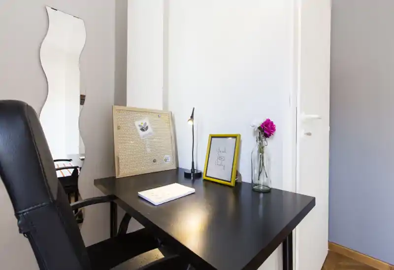 Coin bureau lumineux et soigné avec bureau noir, chaise ergonomique, cadre décoratif et fleurs fraîches — idéal pour le travail ou les études.
