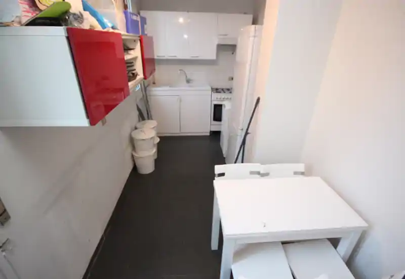 Cuisine en enfilade compacte avec placards blancs, évier, petit four et table pliante — agencement pratique pour un petit appartement.