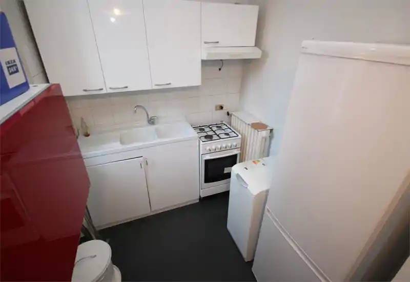 Cuisine compacte et fonctionnelle avec meubles blancs, évier double, cuisinière à gaz et grand réfrigérateur ; espace propre et bien éclairé adapté à un petit appartement.