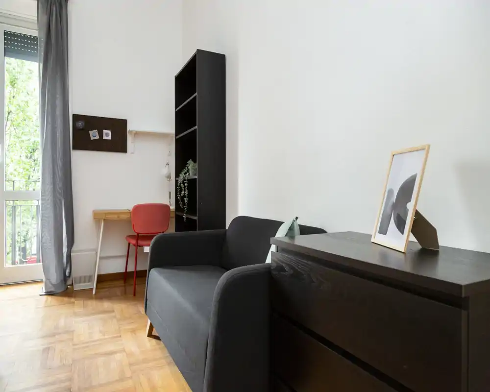 Zona giorno luminosa e compatta con divano, comò e una scrivania vicino alla finestra, perfetta per un monolocale accogliente.