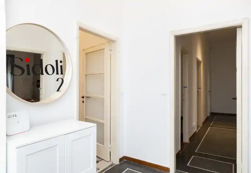 Bright, minimal entrance with a round mirror, white console and doors leading to adjacent rooms — clean and welcoming entryway.
