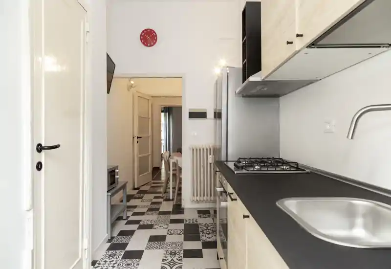 Modern galley kitchen with a black countertop, built-in gas hob and stainless sink; patterned black-and-white floor adds character and a bright, airy feel.