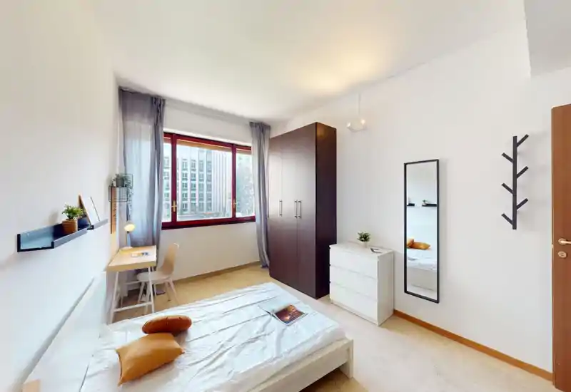 Camera singola luminosa e moderna con letto ben rifatto, scrivania vicino alla finestra e un grande armadio. La luce naturale riempie l’ambiente rendendolo fresco e accogliente.