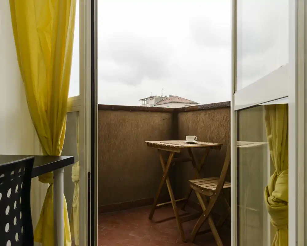 Small private balcony with a wooden bistro table and chairs, ideal for morning coffee; bright yellow curtains add a cheerful accent.