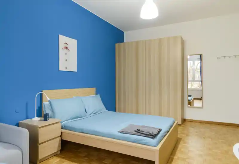 Camera da letto moderna e luminosa con letto matrimoniale con biancheria azzurra, armadio e comodino in legno coordinati; parete accentuata color turchese per un tocco vivace.