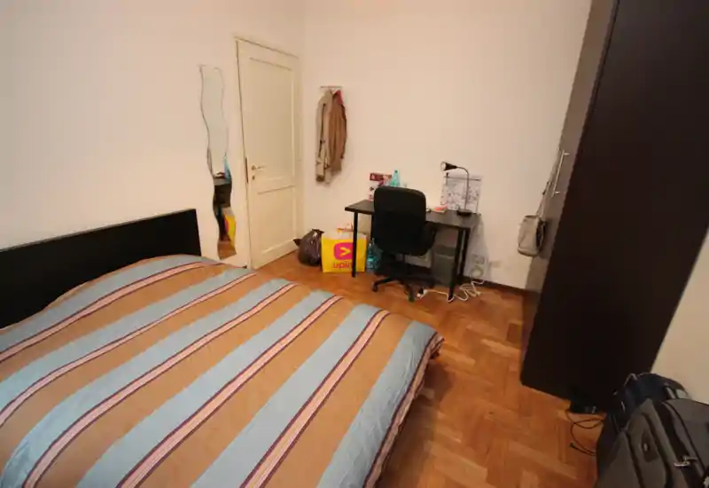 Chambre lumineuse et sobrement meublée avec lit double, bureau et armoire. Parquet et murs neutres pour un espace propre et fonctionnel, idéal pour étudiant ou professionnel.