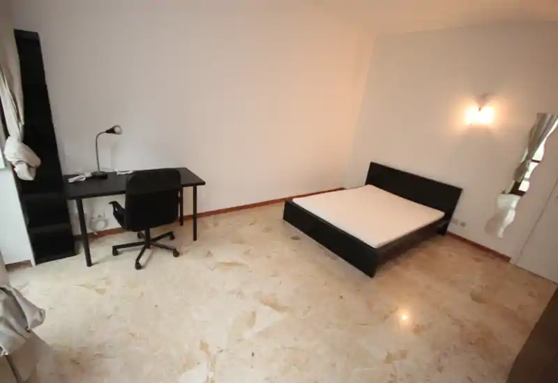 Bright, minimal bedroom with a visible double bed, desk and chair. Marble floor and simple furnishings create a clean, airy space ideal for rental listings.