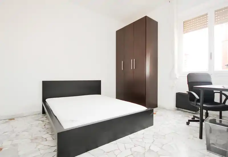 Bright, minimal bedroom with a double bed, wardrobe and a desk by the window. Clean white walls and natural light create a fresh, airy feel suitable for rental listings.