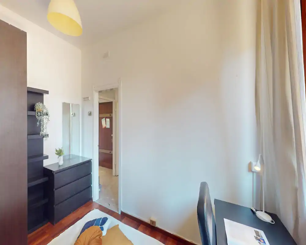 Angolo camera da letto luminoso e ordinato con letto visibile, comò e scrivania vicino alla finestra — soluzione pratica con arredamento moderno e luce naturale soffusa.