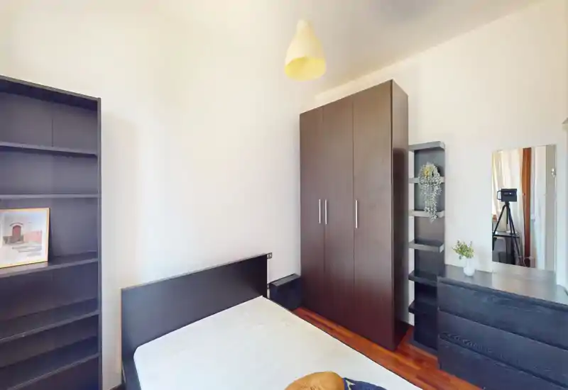 Camera da letto luminosa e minimale con letto ben visibile, armadio in legno scuro e scaffalatura coordinata; pavimento in legno caldo e linee pulite.