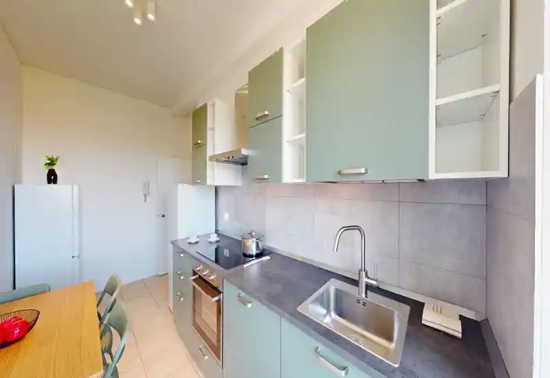 Bright modern kitchen with mint-green cabinets, built-in oven, induction hob and stainless sink; small dining table with chairs visible — practical and well maintained.