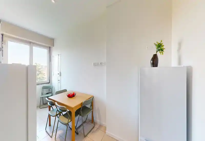 Compact dining area with a wooden table for four and green chairs by a large window providing bright natural light; simple decor with a decorative bowl makes it inviting.