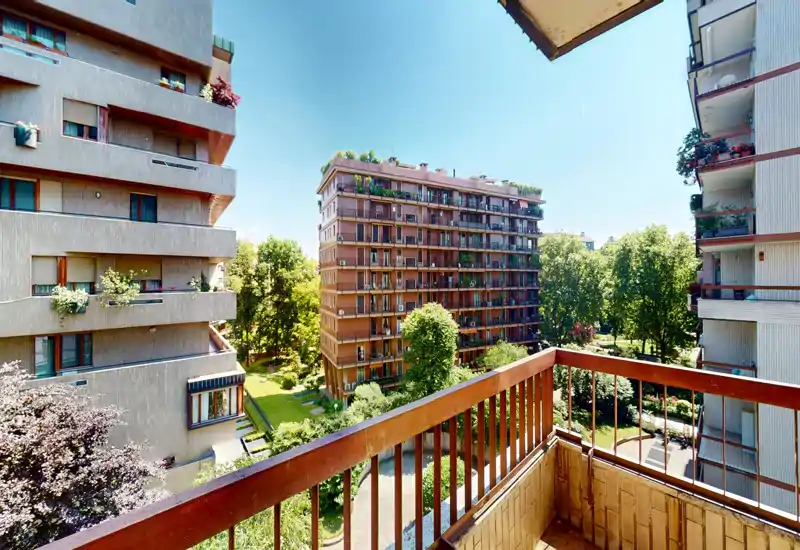 Sunny private balcony overlooking a green courtyard and neighboring apartment buildings; ideal for morning coffee and city views.