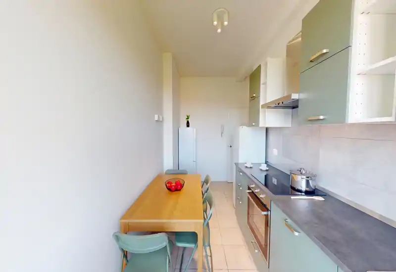 Compact modern kitchen with mint-green cabinets, a dark countertop, built-in oven and an adjacent wooden dining table with chairs — bright, functional and neatly arranged for small-space living.