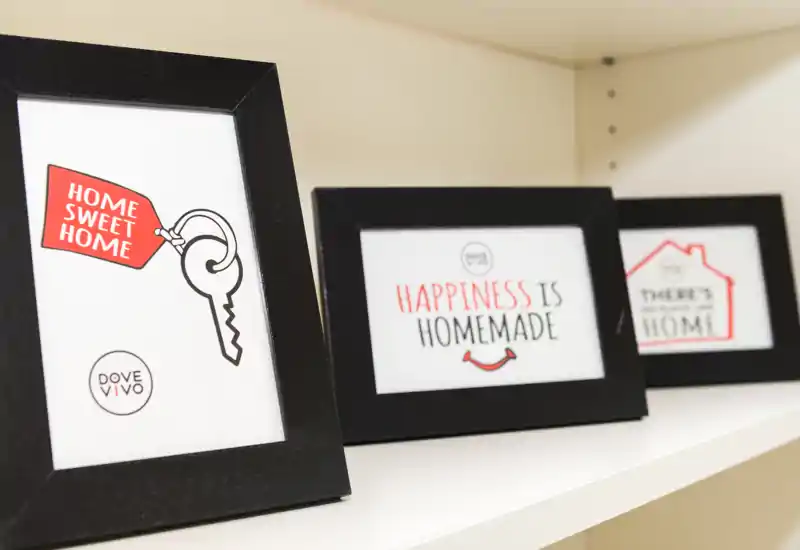 Primer plano de una estantería decorativa con tres marcos que dicen «Home Sweet Home» y «Happiness is Homemade», creando una composición acogedora para la entrada.