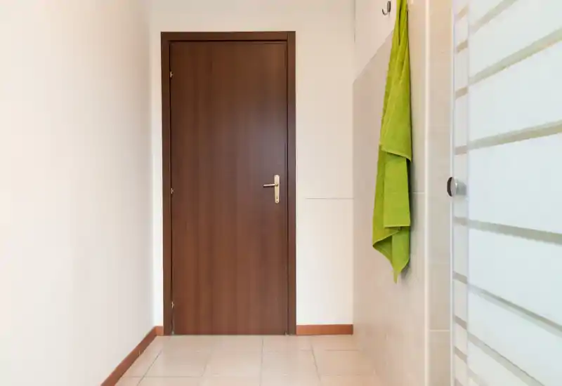 Simple entrance/hallway with a wooden interior door, tiled floor and a towel hanging on the wall; neutral lighting makes it suitable for a listing photo.