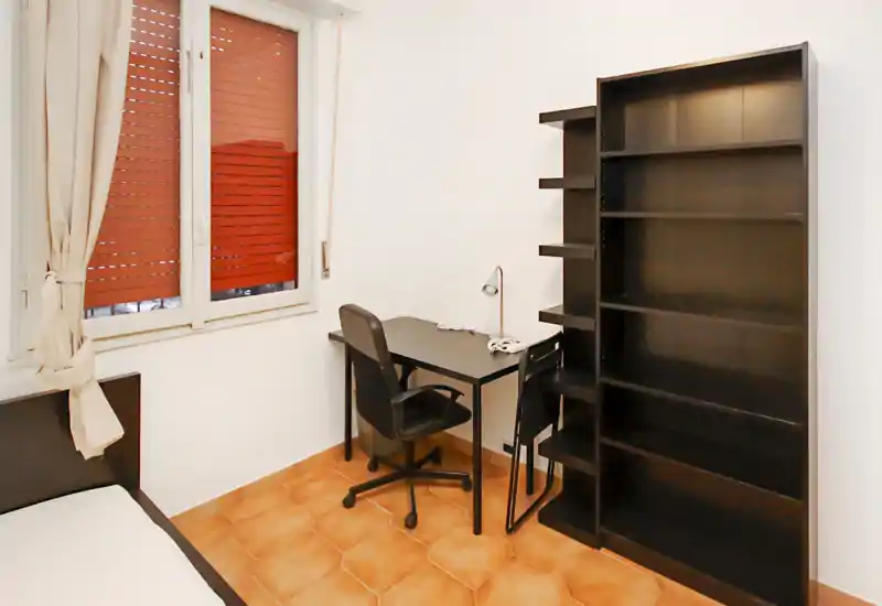Camera semplice con letto singolo, scrivania compatta e scaffalatura — luminosa, ordinata e funzionale per studenti o soggiorni brevi.