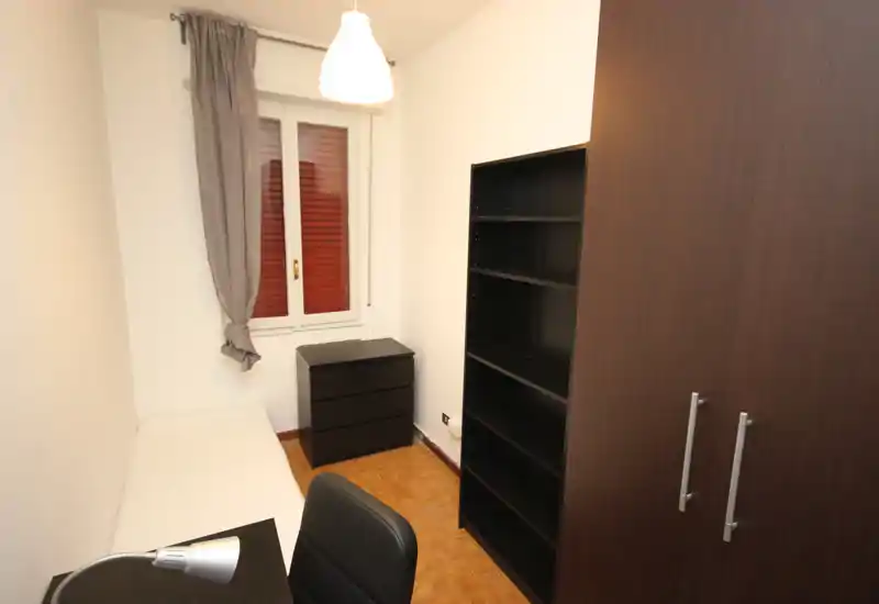 Habitación individual compacta con cama, cómoda, estantería y armario; decoración neutra y lámpara de techo que ofrecen un espacio luminoso y ordenado, ideal para estudiante o una sola persona.