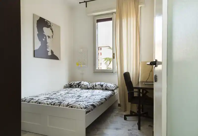 Chambre lumineuse et bien mise en scène avec un lit double, une literie à motif et un petit espace bureau près de la fenêtre laissant entrer la lumière naturelle.