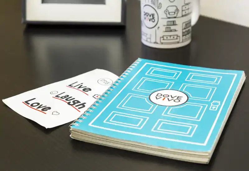 Close-up of a tabletop with a spiral notebook, a printed note and a mug — a detail shot without a clear room context.