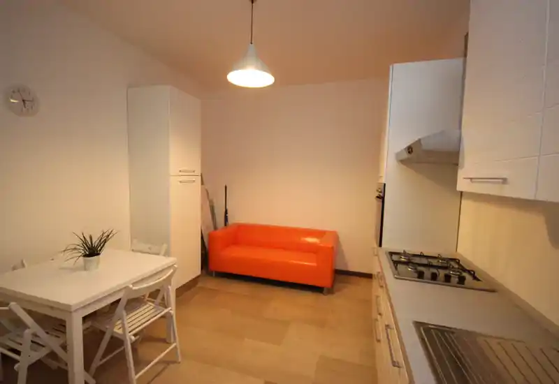 Compact kitchen with integrated stovetop and sink, a small dining table and a bright orange sofa adding a pop of color and character.