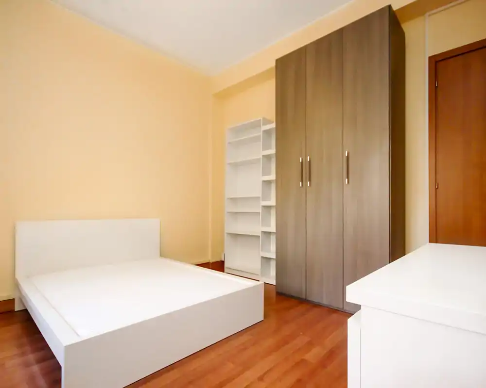 Bright, modern bedroom with a low white bedframe, wooden wardrobe and shelving; minimal, clean styling ideal for rental listing photos.