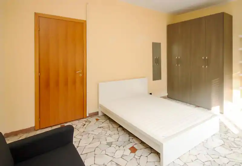 Dormitorio sencillo y luminoso con cama blanca, gran armario y luz natural. Decoración mínima y tonos neutros que ofrecen un espacio limpio y funcional, perfecto para anuncios de alquiler.
