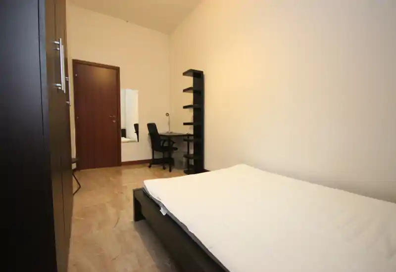 Dormitorio sencillo y bien iluminado con cama doble en estructura de madera oscura, escritorio y estantería en la pared trasera. Paredes neutras y suelo tipo mármol que aportan una atmósfera limpia y minimalista ideal para un anuncio.