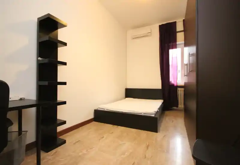Dormitorio compacto y moderno con cama baja, estantería simple y armario. Espacio luminoso y minimalista, apto para una persona o pareja.