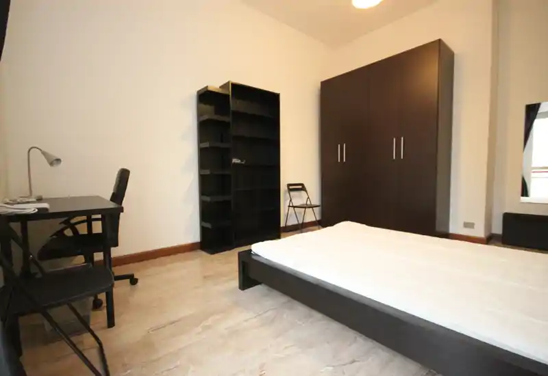 Bright, minimalist bedroom with a low wooden bed frame, wardrobe and desk — clean lines and good natural light create a simple, functional space.