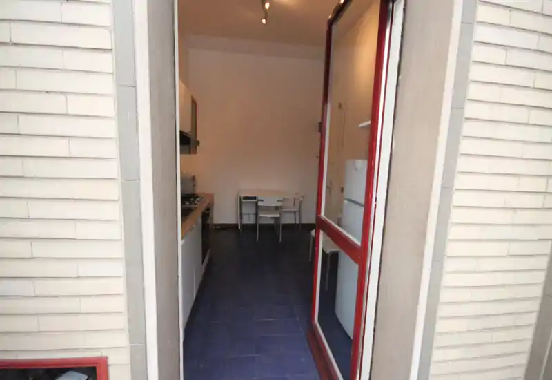 Compact galley kitchen viewed from the entrance, with a stove and countertop on the left and a small dining nook at the back. Functional layout suitable for a small apartment.