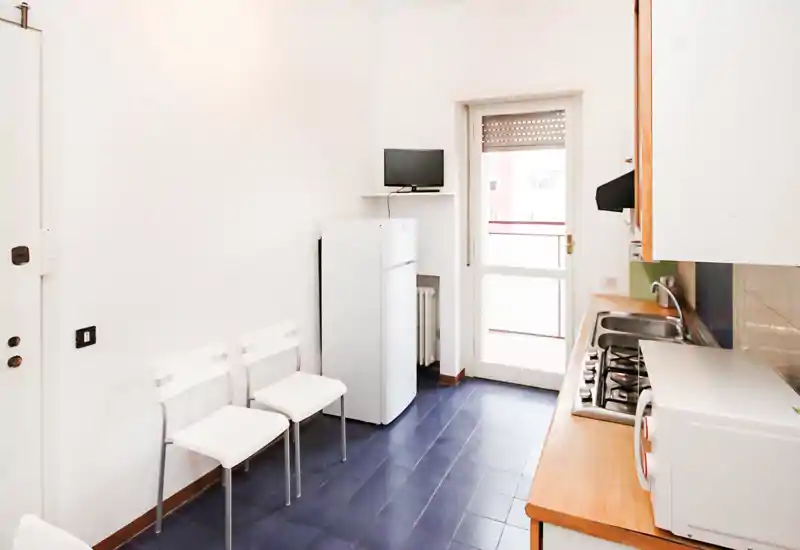 Bright compact kitchen with a gas hob, sink and small appliances, white cabinets and a balcony door that brings natural light. Functional layout ideal for a studio or small apartment.