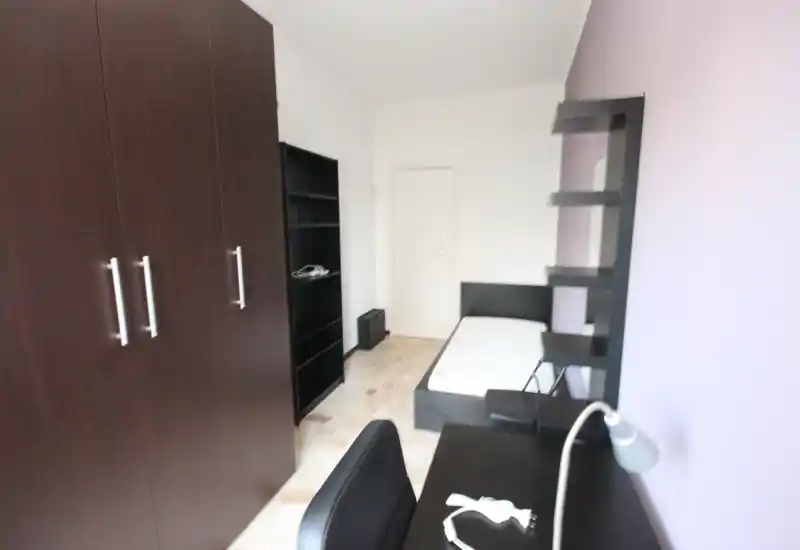 Dormitorio luminoso y compacto con cama individual, mobiliario de madera oscura y estanterías empotradas. Dispone de mesa de trabajo y armario amplio, ideal para una persona.