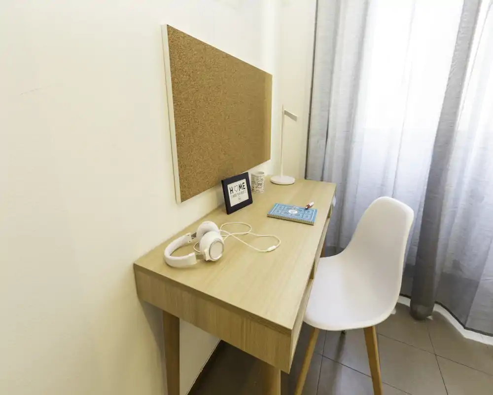 Angolo studio luminoso e minimale con scrivania in legno, sedia bianca, bacheca in sughero e lampada da tavolo — perfetto per lavorare o studiare in uno spazio compatto.
