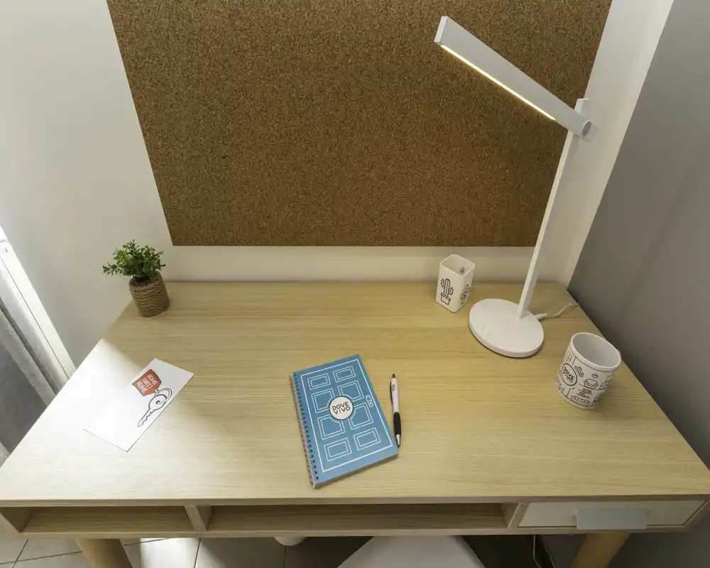 Tidy desk workspace with a cork noticeboard, desk lamp, notebook and small plant — ideal photo to show a study or compact workspace corner.
