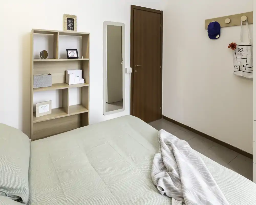 Bright, tidy bedroom featuring a large bed in the foreground, a wooden shelving unit and a full-length mirror by the door — minimalist, comfortable decor ideal for rental photos.