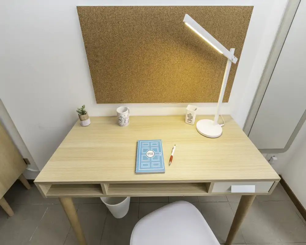Area studio/angolo scrivania ordinato con scrivania in legno chiaro, lampada da tavolo, bacheca in sughero e piccoli accessori — spazio luminoso e pulito ideale per lavoro o studio.