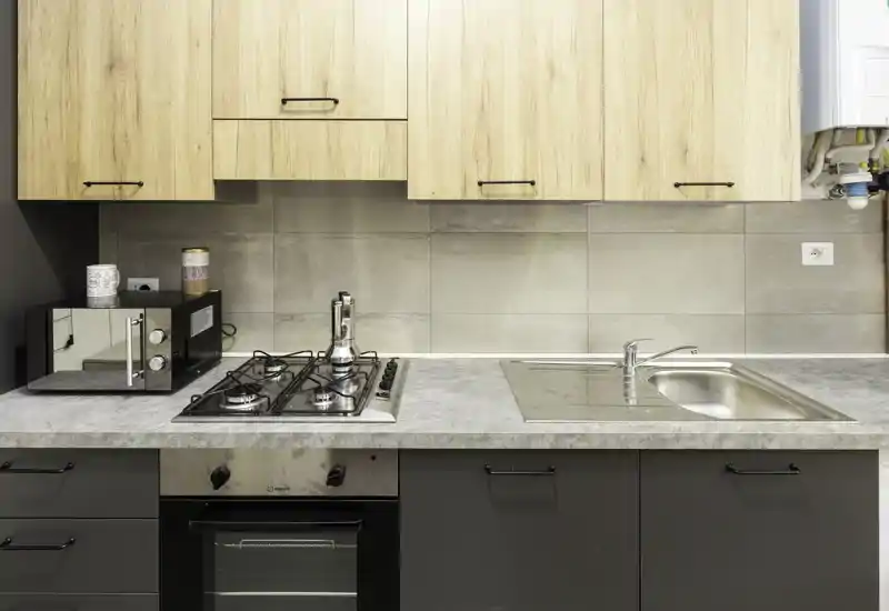 Cucina moderna compatta con piano cottura a gas, forno incassato, lavello in acciaio e pensili in legno. Piano di lavoro pulito e disposizione efficiente, perfetta per affitti brevi.