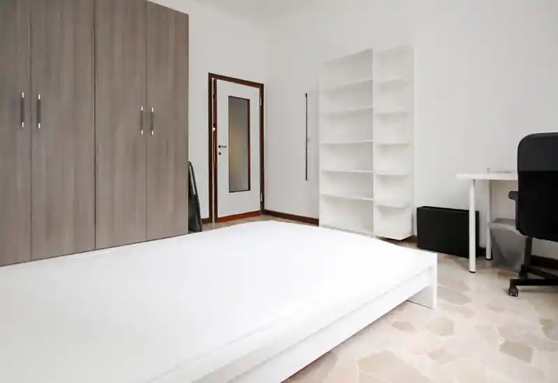 Dormitorio minimalista con cama baja blanca, gran armario y estanterías. Espacio luminoso y ordenado, perfecto para destacar almacenaje y luz natural.