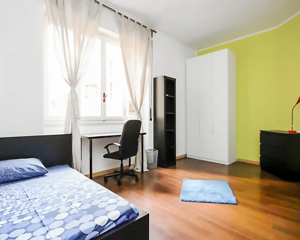 Dormitorio moderno y luminoso con cama doble, escritorio junto a la ventana, armario y mobiliario minimalista — ideal para estudiantes o profesionales.