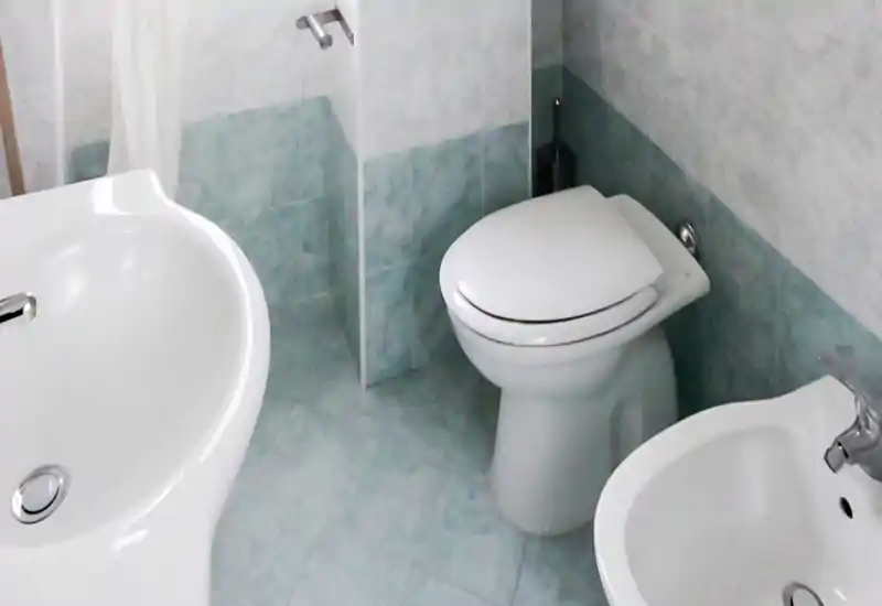 Baño compacto y limpio con inodoro, bidé y lavabo sobre azulejos verde claro; luminoso y bien cuidado.
