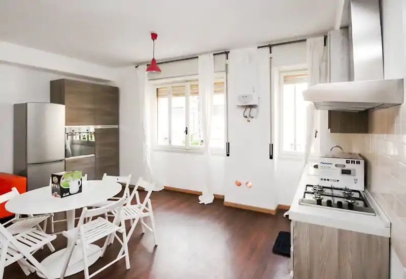 Cocina moderna y luminosa con electrodomésticos de acero, placa de gas y zona de comedor contigua con mesa redonda y sillas plegables — ideal para pisos pequeños.