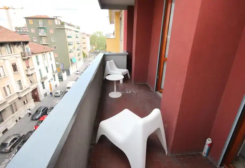 Balcón urbano estrecho con sillas blancas modernas y una mesa redonda pequeña, con vistas a la calle residencial — espacio exterior luminoso y funcional.