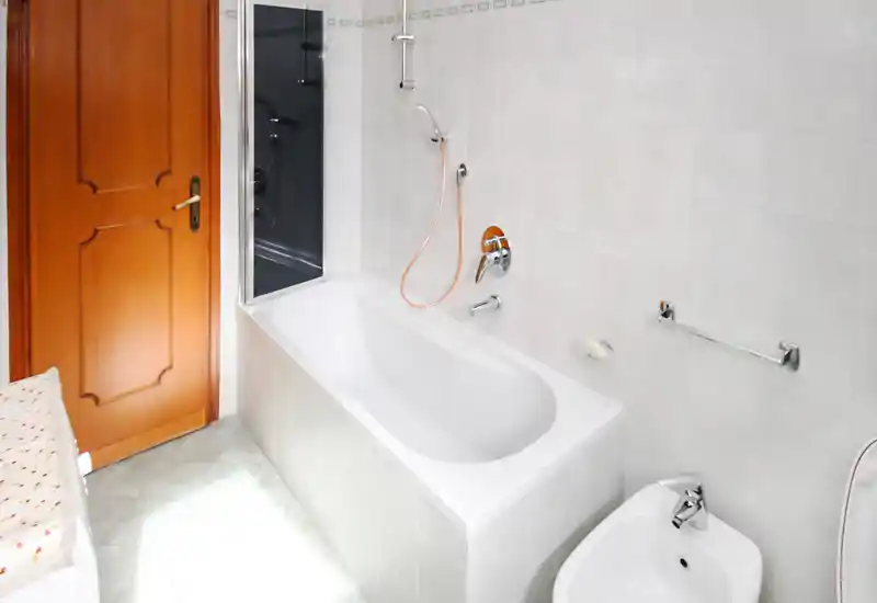 Baño luminoso y limpio con bañera y ducha de mano; azulejos claros y grifería cromada crean un espacio ordenado y funcional.