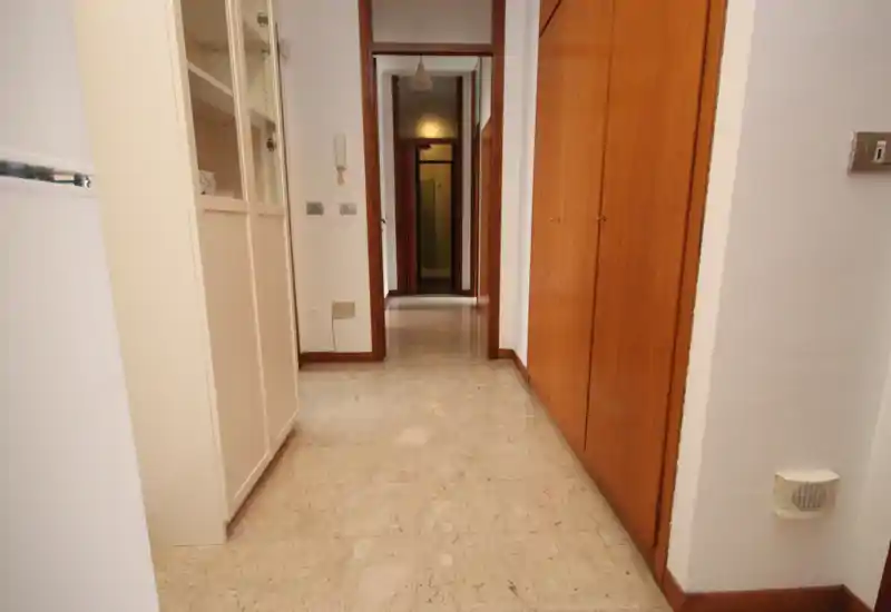 Pasillo luminoso con suelo de mármol y armarios empotrados de madera — vista clara de la entrada que conduce a las habitaciones interiores.